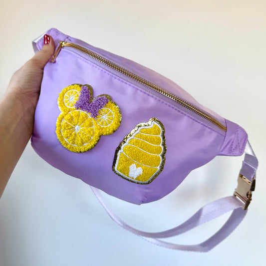 Purple fanny pack with yellow and purple decorative elements held by a hand on a light background